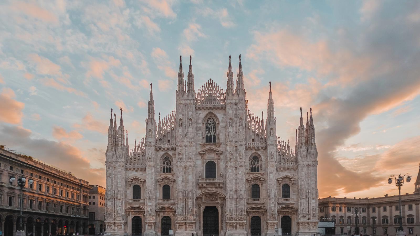 a large white building with many spires and people walking in front with Milan Cathedral in the background