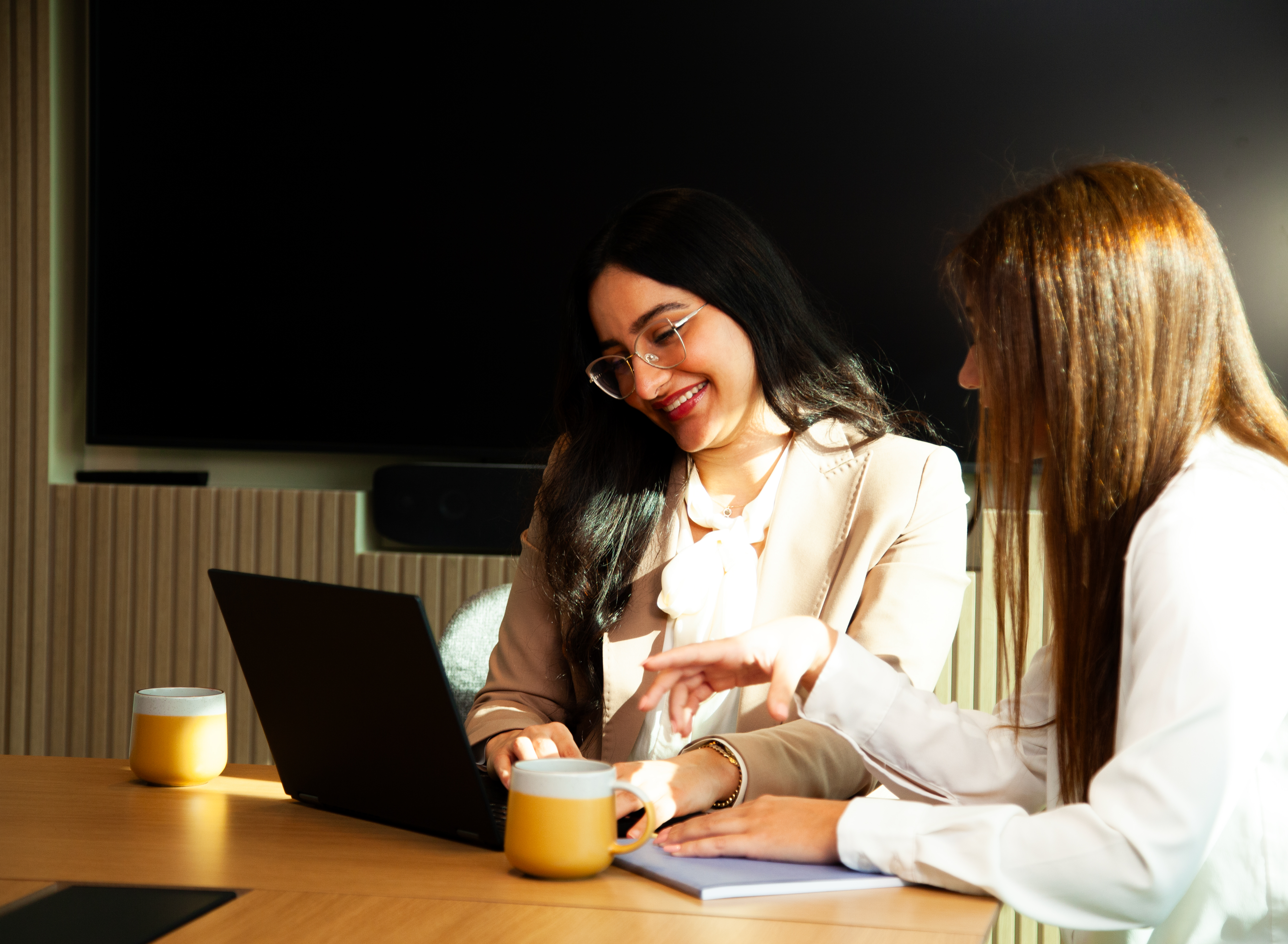 two women sitting at a table with a laptop