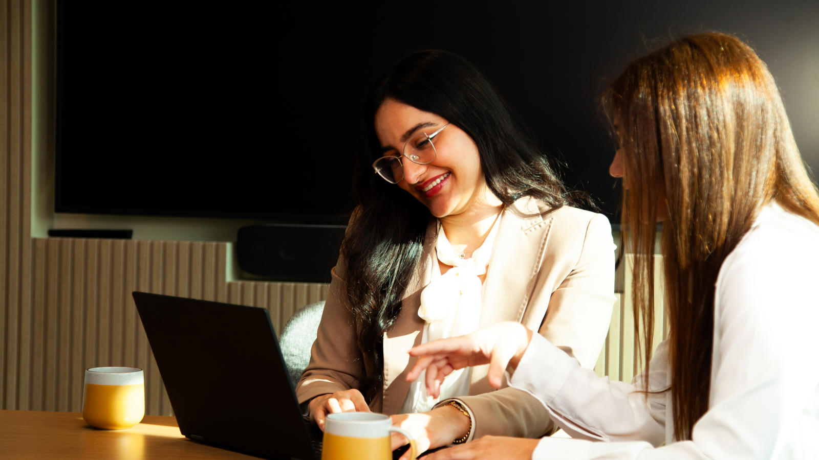 two women sitting at a table with a laptop
