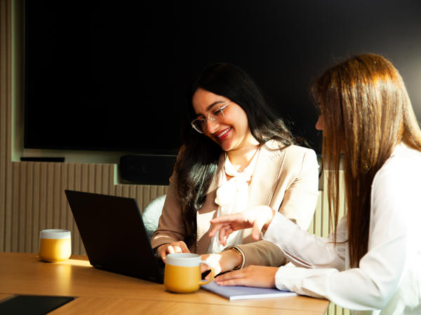 two women sitting at a table with a laptop