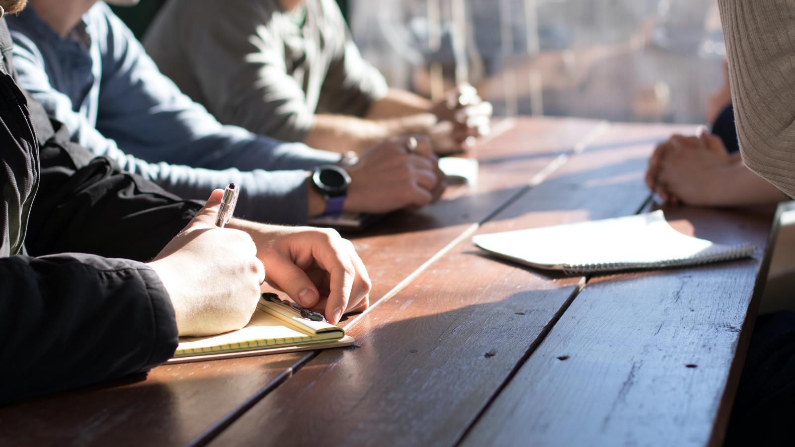 a group of people sitting at a table writing on notebooks