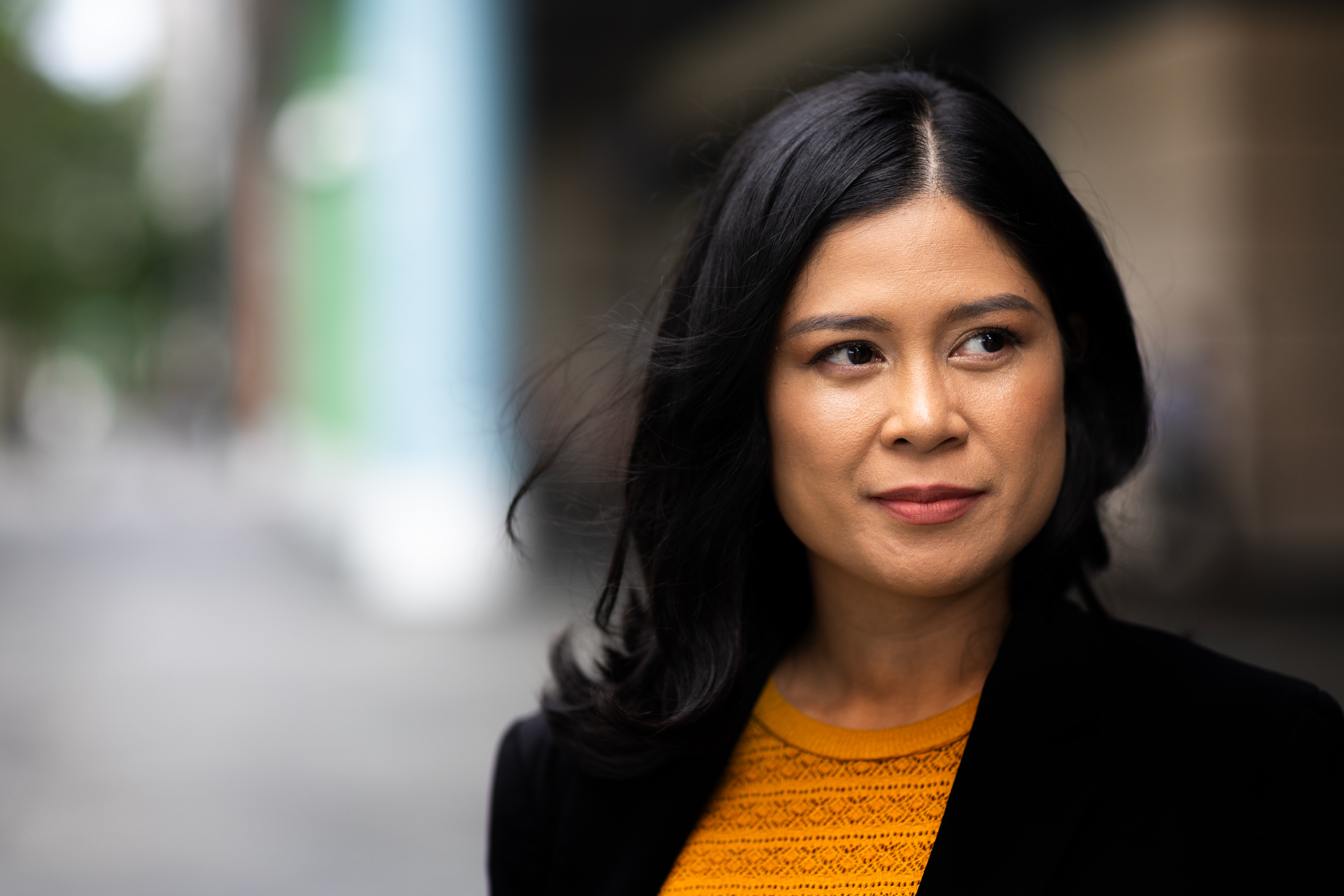 a woman with dark hair wearing a yellow shirt and black jacket