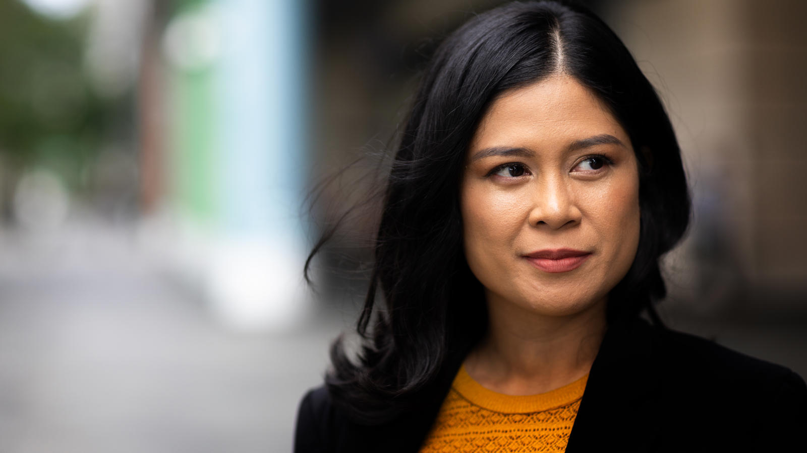 a woman with dark hair wearing a yellow shirt and black jacket