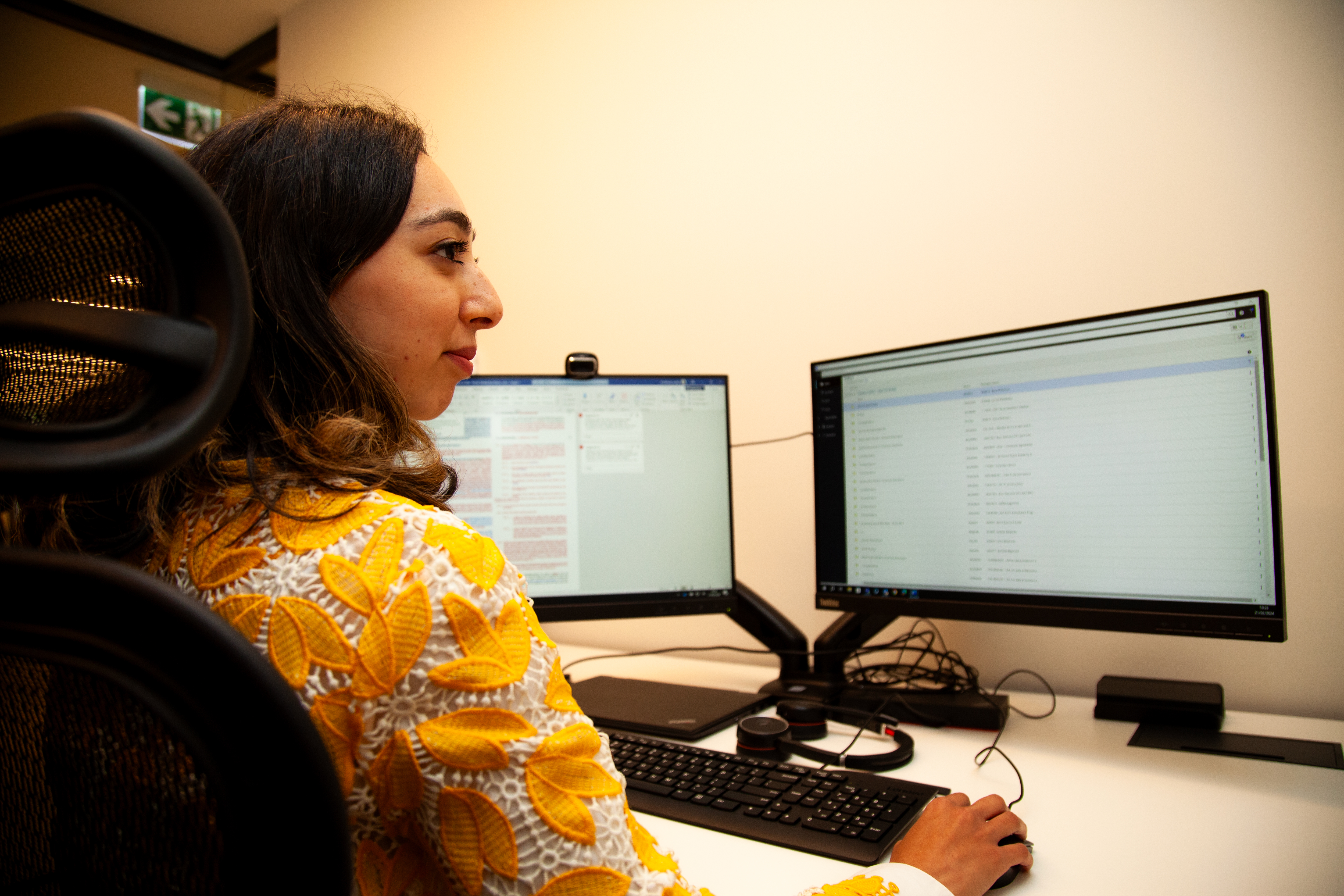 a woman sitting at a desk with two computers